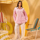 Woman in a pink shirt and white pants standing in a colorful beach-themed setting with chairs and an umbrella.