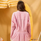 Person wearing a pink striped shirt against a yellow background with a surfboard and umbrella.