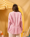 Person wearing a pink striped shirt against a yellow background with a surfboard and umbrella.