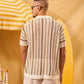 Man wearing a patterned shirt and sunglasses standing under a yellow and white striped umbrella.