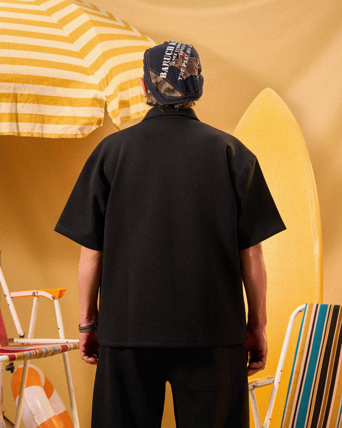 Person wearing a black shirt and cap with a yellow and white striped umbrella in the background
