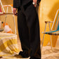 Person wearing a black suit with a yellow background and vintage furniture.