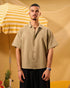 Man wearing a beige shirt and black pants standing next to a yellow and white striped umbrella on a yellow background.