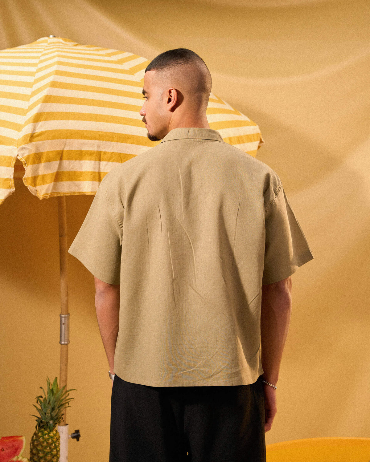 Man wearing a beige shirt standing next to a yellow and white striped umbrella on a yellow background