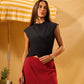 Woman in black top and red skirt standing under a yellow and white striped umbrella with a pineapple on a table.