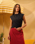 Woman in black top and red skirt standing under a yellow and white striped umbrella with a pineapple on a table.