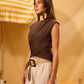 Woman in a brown top and beige pants standing under a striped umbrella with a yellow background