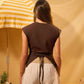 Person wearing a brown top and beige pants with a yellow and white striped umbrella in the background.