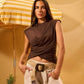 Woman in a brown top and beige pants standing under a yellow and white striped umbrella with a pineapple and watermelon on a yellow background.