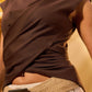 Person wearing a brown sleeveless top with a beige belt against a yellow background