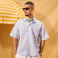Man wearing sunglasses and a light blue shirt with a colorful collar against a yellow background