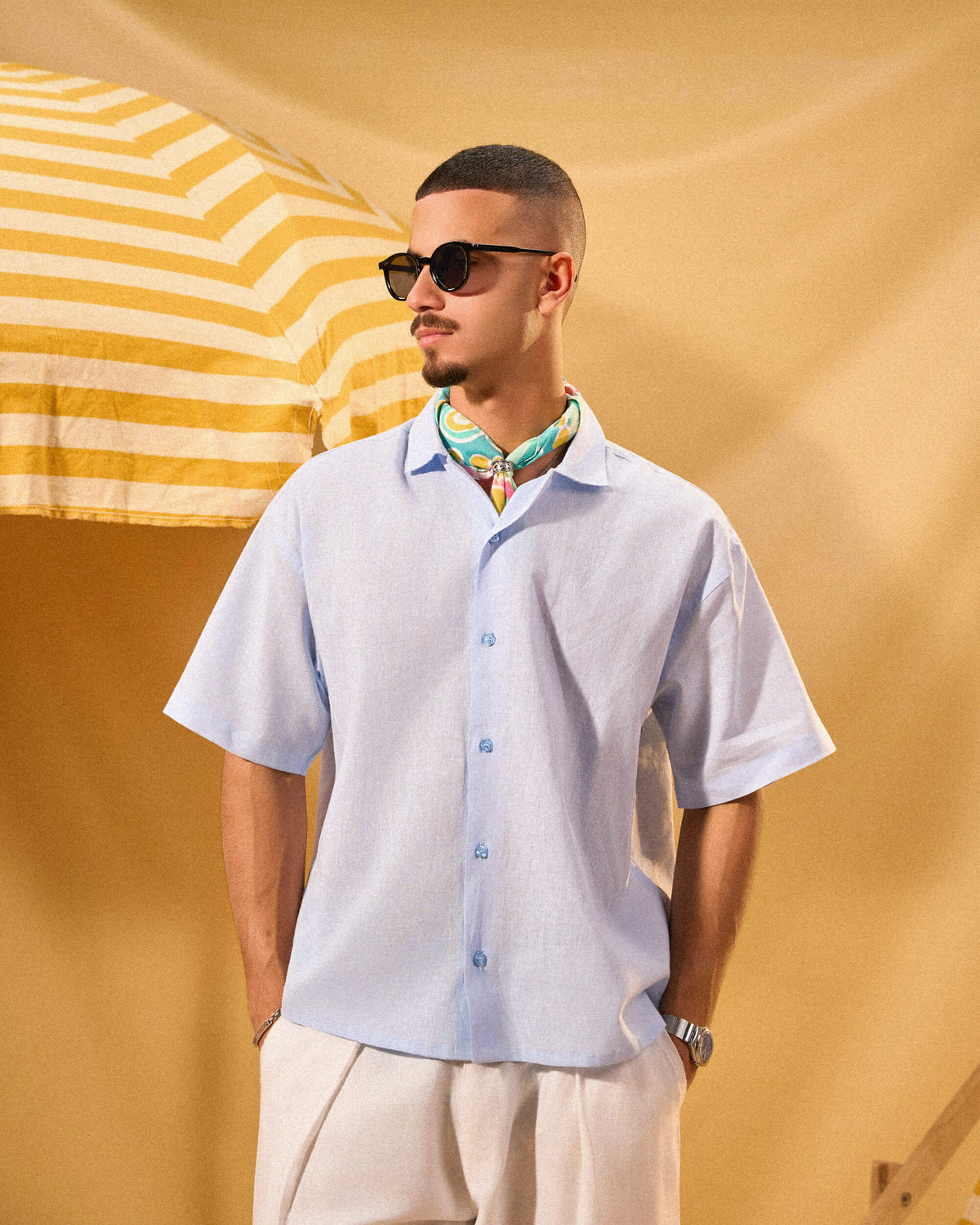 Man wearing sunglasses and a light blue shirt with a colorful collar against a yellow background
