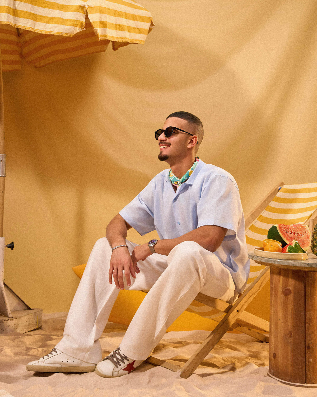 Man sitting on a beach chair under a striped umbrella with a yellow sand background