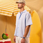 Man standing next to a surfboard with a yellow and white striped umbrella and watermelon in the background.