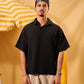 Man wearing a black shirt and beige pants standing against a yellow background with an umbrella.