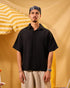 Man wearing a black shirt and beige pants standing against a yellow background with an umbrella.