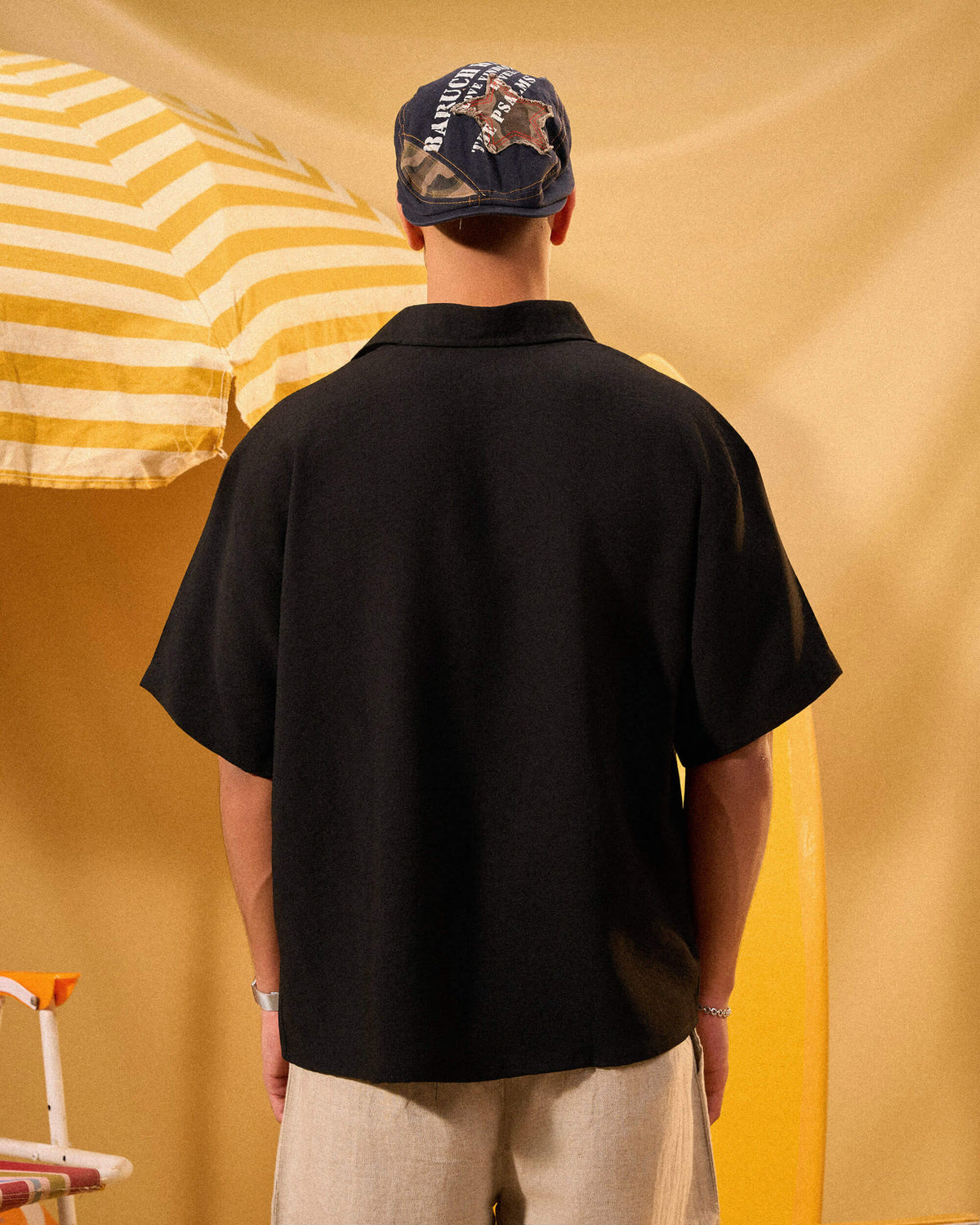 Person wearing a black shirt and camouflage cap against a yellow and white striped background
