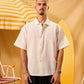 Man wearing a white shirt standing next to a yellow surfboard and striped umbrella on a yellow background