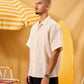 Man in a white shirt standing next to a yellow surfboard and striped umbrella on a yellow background