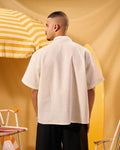 Man wearing a beige shirt standing in front of a yellow and white striped umbrella.