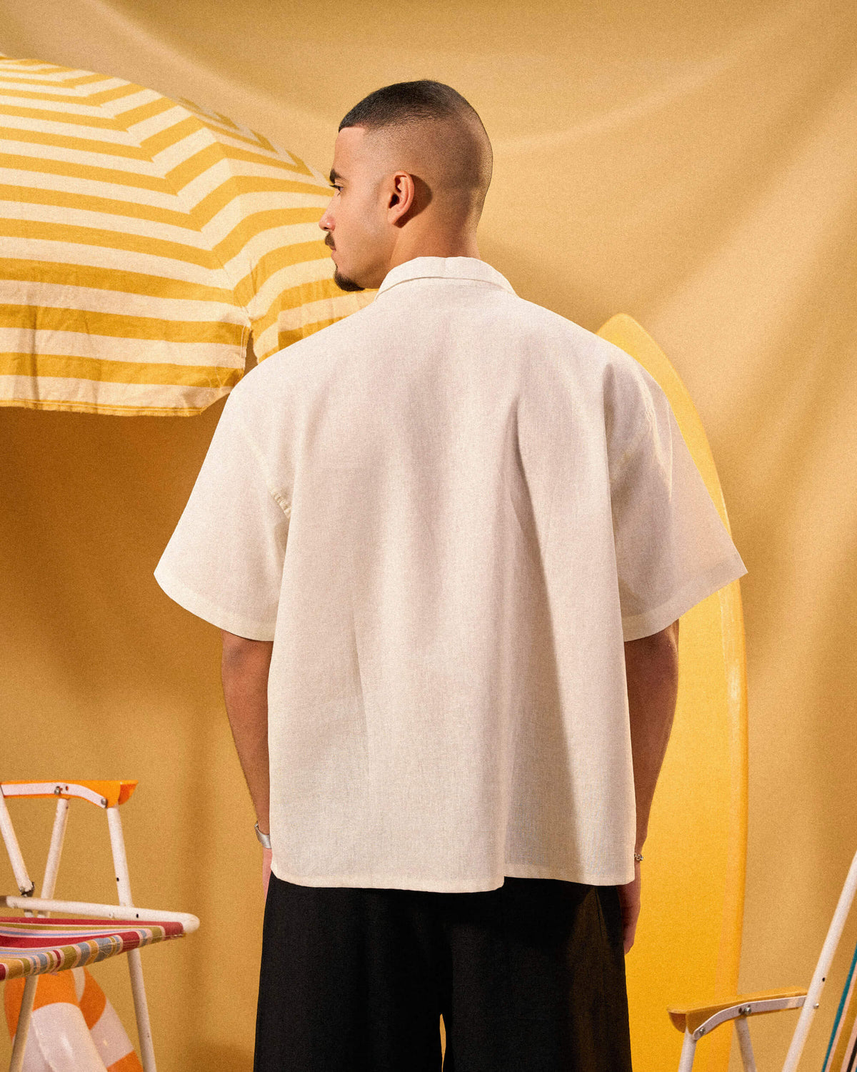 Man wearing a beige shirt standing in front of a yellow and white striped umbrella.