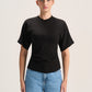 A woman modeling a black short-sleeve crewneck t-shirt paired with light blue jeans, standing against a plain light beige studio background.