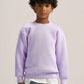 A child model wearing a light purple crewneck sweatshirt, a white t-shirt, and blue jeans, standing against a plain light beige studio background.