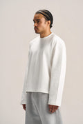 a man showing his side profile wearing a white long sleeves boxy t-shirt on an ash grey sweatpants with a solid background  