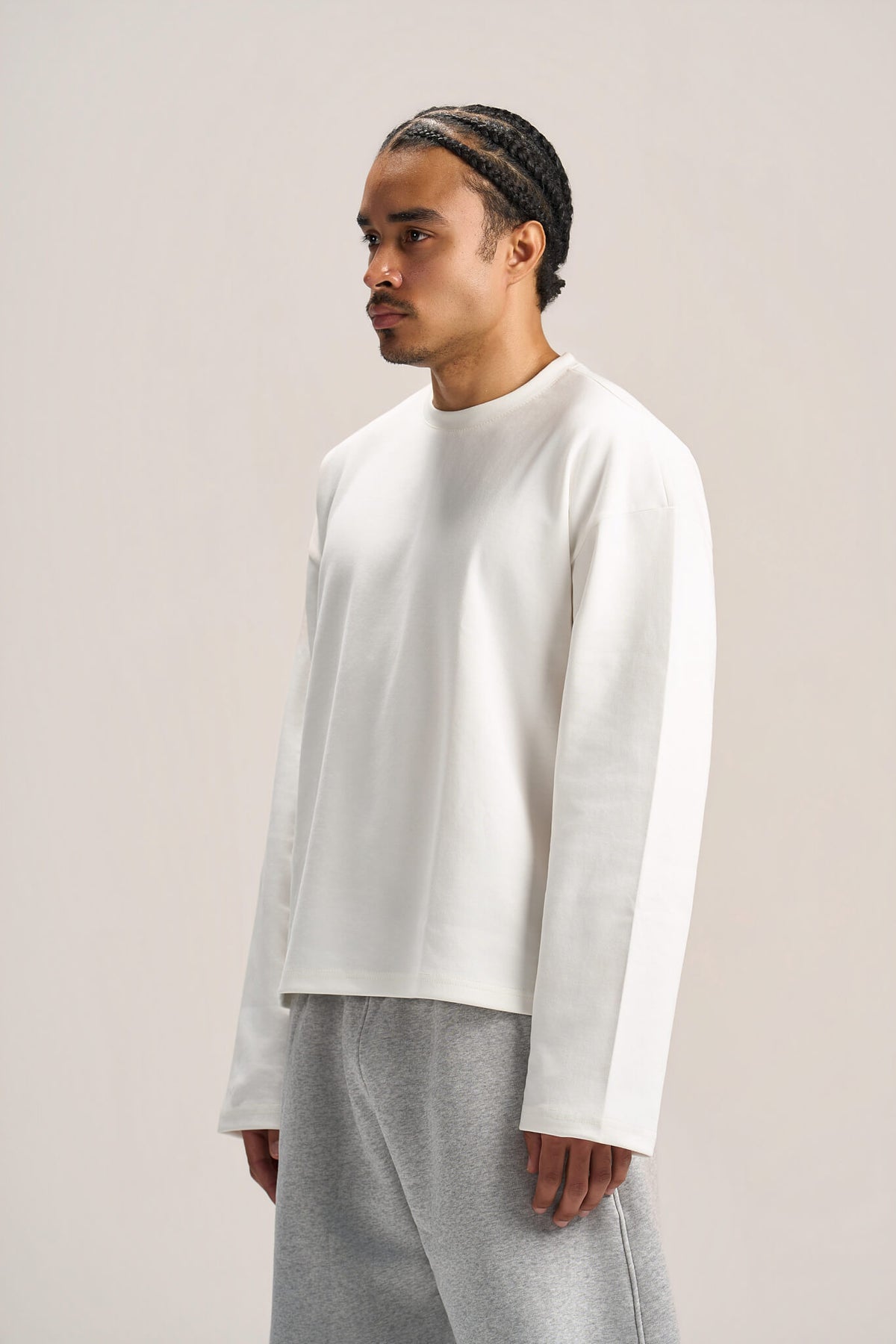 a man showing his side profile wearing a white long sleeves boxy t-shirt on an ash grey sweatpants with a solid background  