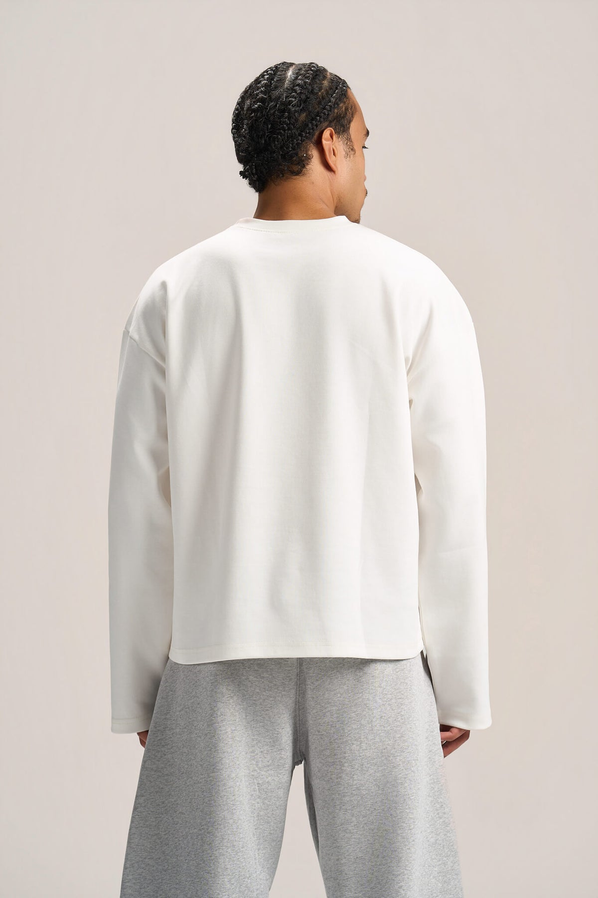 a man showing his back profile wearing a white long sleeves boxy t-shirt on an ash grey sweatpants with a solid background  