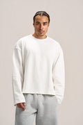 a man wearing a white long sleeves boxy t-shirt on an ash grey sweatpants with a solid background