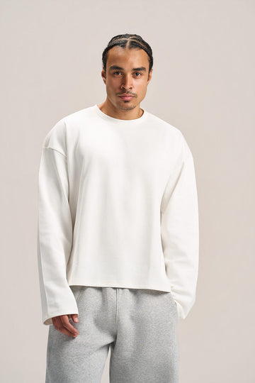a man wearing a white long sleeves boxy t-shirt on an ash grey sweatpants with a solid background