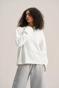 a woman wearing a white long sleeves boxy t-shirt on a ash-grey sweatpants with a solid background