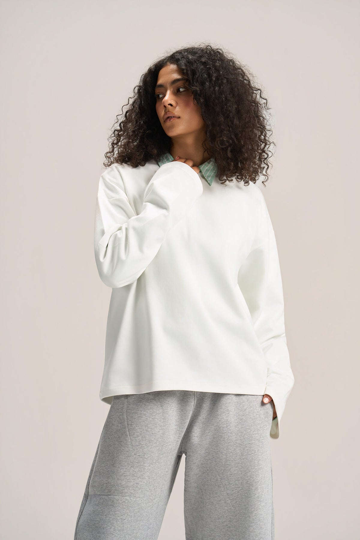 a woman wearing a white long sleeves boxy t-shirt on a ash-grey sweatpants with a solid background