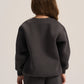 A model shown from the back wearing a dark charcoal gray crewneck sweatshirt and matching dark gray sweatpants against a light gray studio background.