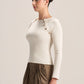 A woman modeling a fitted long-sleeve cream top with decorative gold-toned buttons along the neckline, paired with brown draped trousers, against a plain light beige studio background.
