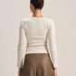 A woman shown from the back wearing a fitted cream ribbed long-sleeve top and brown wide-leg pants against a plain light beige studio background.