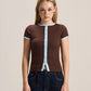 A woman modeling a brown short-sleeve ribbed knit top with light blue trim details, paired with dark blue jeans, against a solid light beige background.