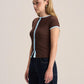 A woman modeling a brown short-sleeve knit top with light blue trim along the collar, front opening, and sleeve cuffs, paired with dark wide-leg jeans against a plain light beige studio background.