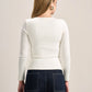 A woman shown from the back wearing a fitted off-white long-sleeve top and dark blue jeans against a plain light beige studio background.
