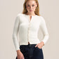 A woman modeling a fitted long-sleeve cream knit cardigan with a split neckline and front buttons, paired with dark blue jeans, against a plain light beige studio background.