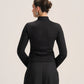 A woman shown from the back wearing a black long-sleeve mock-neck top and matching black skirt against a plain light gray studio background.