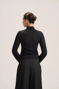 A woman shown from the back wearing a black long-sleeve mock-neck top and matching black skirt against a plain light gray studio background.