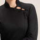 A close-up of a model wearing a black long-sleeve top with a mock neck and decorative black lace applique details across the chest.