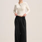 A woman modeling a cream ribbed long-sleeve cropped cardigan and black wide-leg trousers against a plain light beige studio background.
