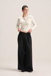 A woman modeling a cream ribbed long-sleeve cropped cardigan and black wide-leg trousers against a plain light beige studio background.