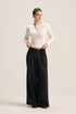 A woman modeling a cream ribbed long-sleeve cropped cardigan and black wide-leg trousers against a plain light beige studio background.