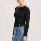 A woman modeling a black long-sleeve button-front top with a small front slit, paired with blue jeans, against a plain light background.