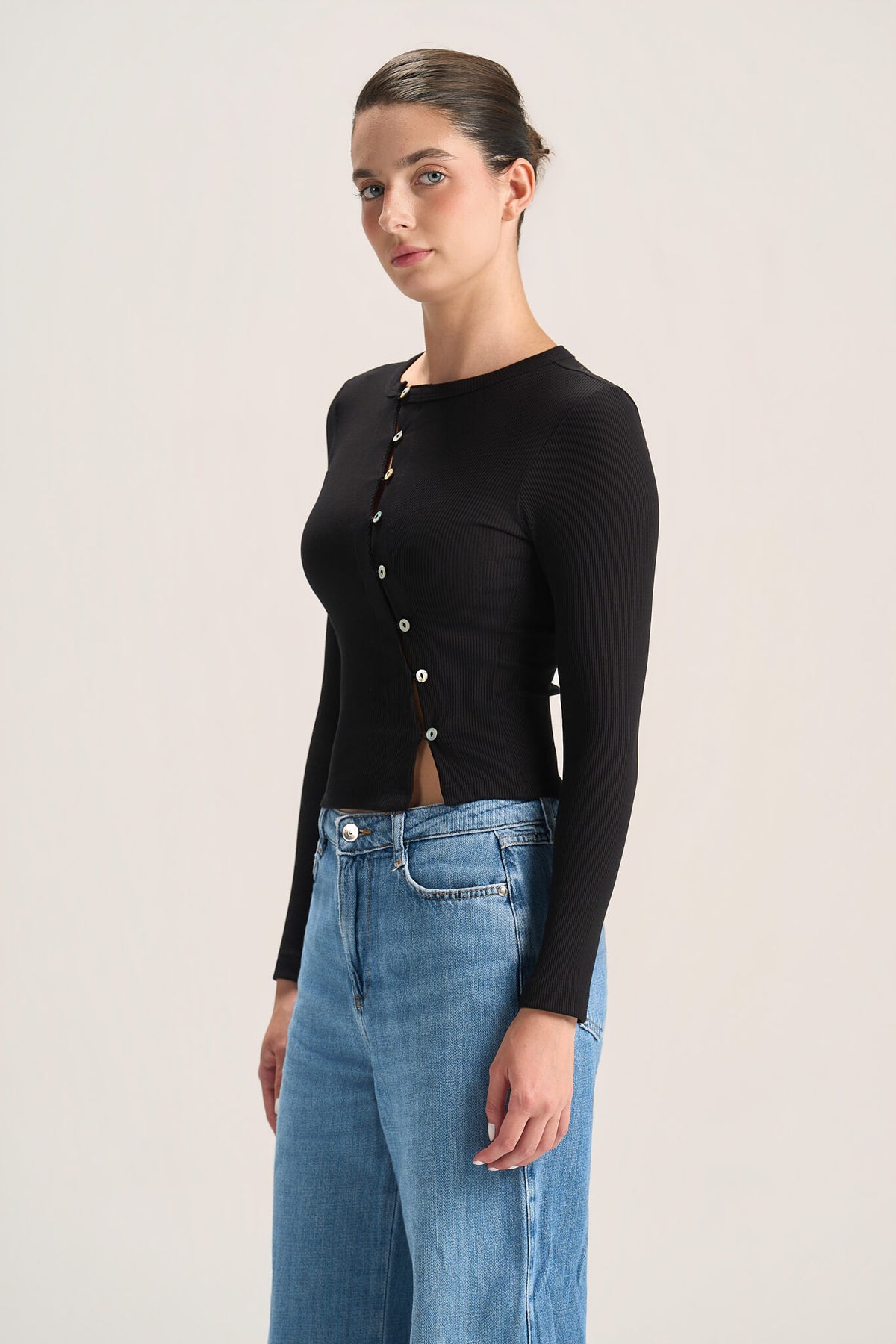 A woman modeling a black long-sleeve button-front top with a small front slit, paired with blue jeans, against a plain light background.
