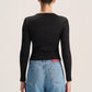 A woman shown from the back wearing a fitted black long-sleeve top and light blue jeans against a plain light background.